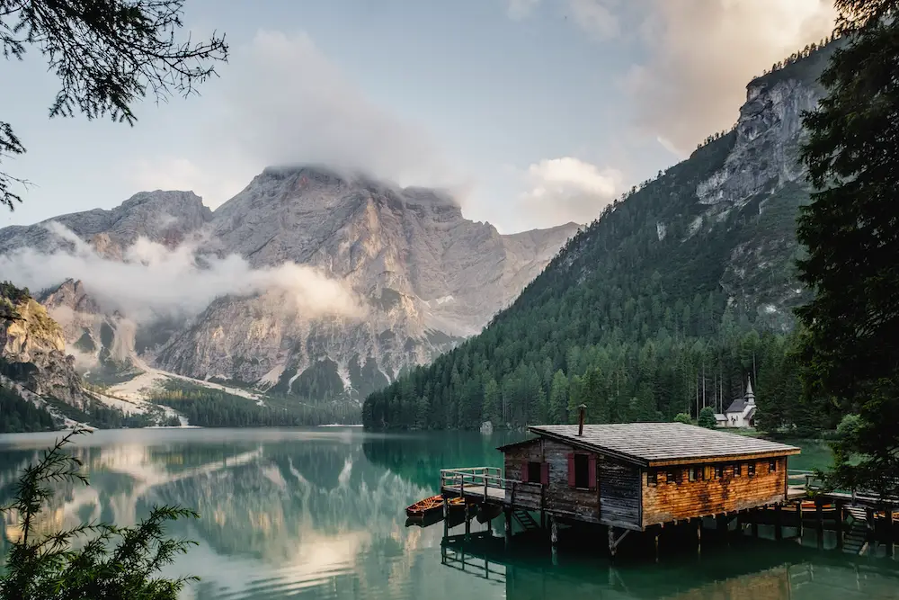 A log cabin lakehouse and dock on Lago di Braies with the snow-capped mountains in the background Lago di braies italy